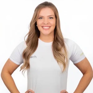 Lächelnde Frau mit langen blonden Haaren in einem weißen T-Shirt, die Hände in die Hüften gestemmt vor einem weißen Hintergrund.