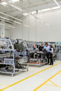 Drei Personen unterhalten sich in einem hellen, modernen Industriearbeitsbereich in der Nähe von Maschinen über „Führung in der Produktion“.