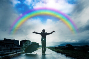 Eine Person steht mit ausgestreckten Armen unter einem Regenbogen, ein Regenschirm liegt auf dem Boden – ein Bild, das eine Insights MDI®-Analyse widerspiegelt.